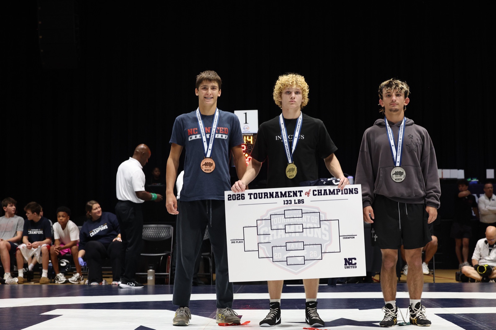 The 133 lb podium at the 2026 Tournament of Champions — the three placers on the mat, the champion holding the bracket