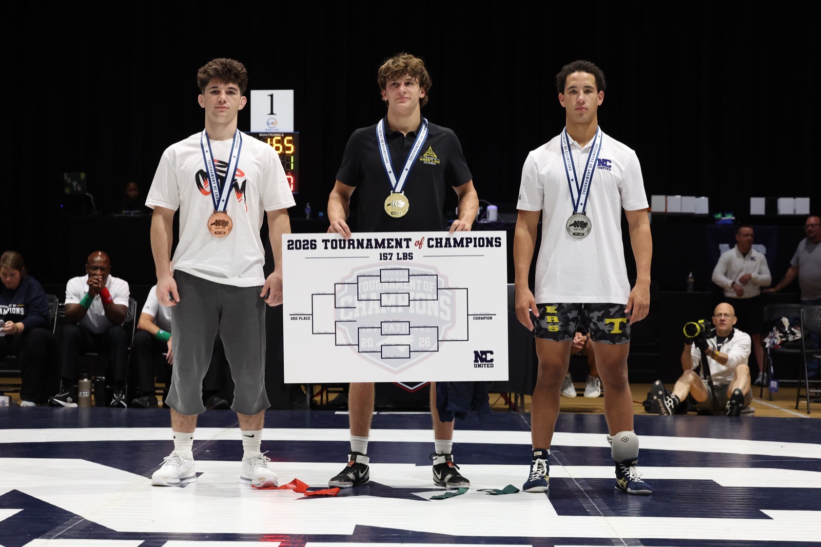 The 157 lb podium at the 2026 Tournament of Champions — the three placers on the mat, the champion holding the bracket