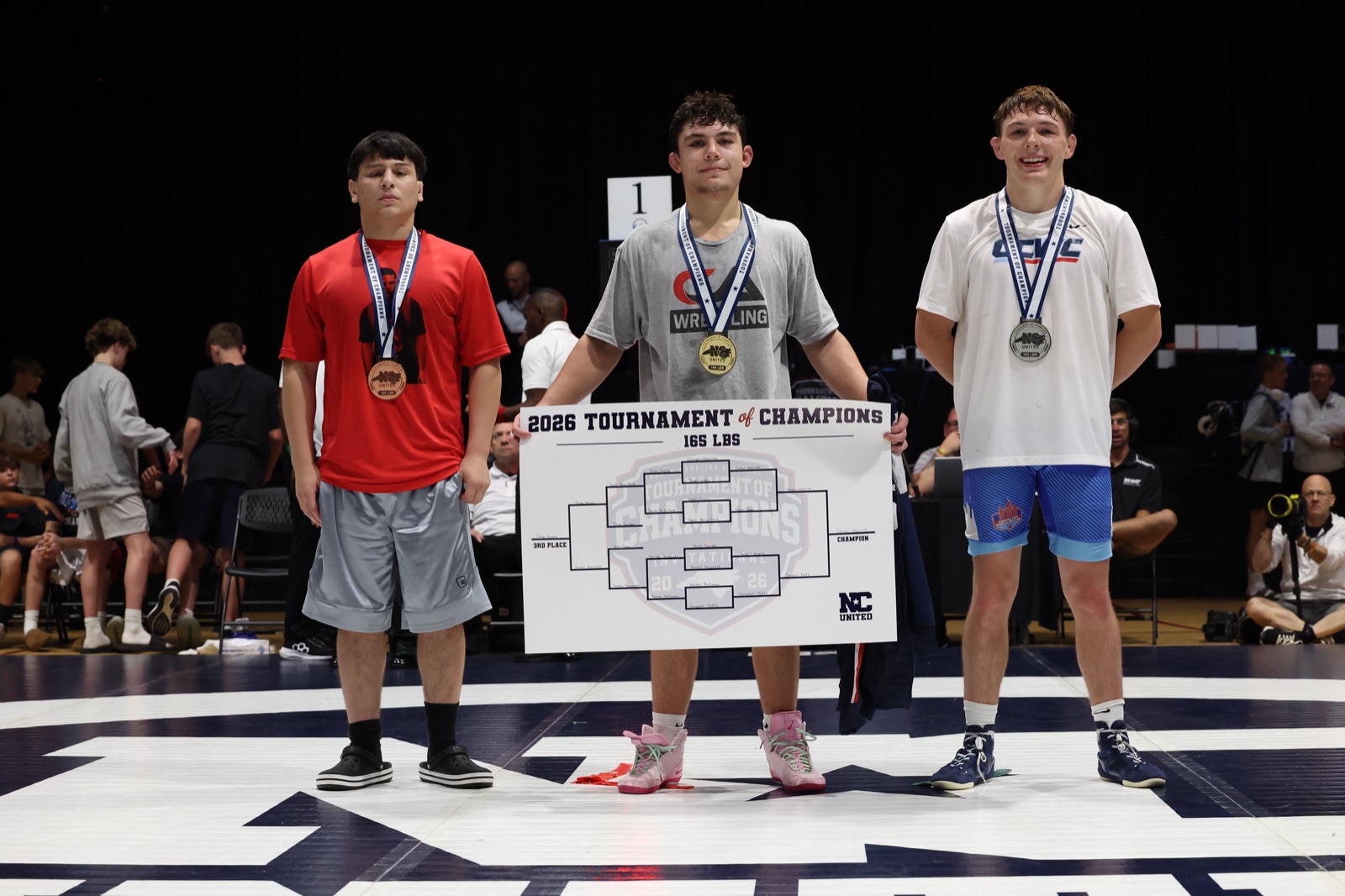 The 165 lb podium at the 2026 Tournament of Champions — the three placers on the mat, the champion holding the bracket